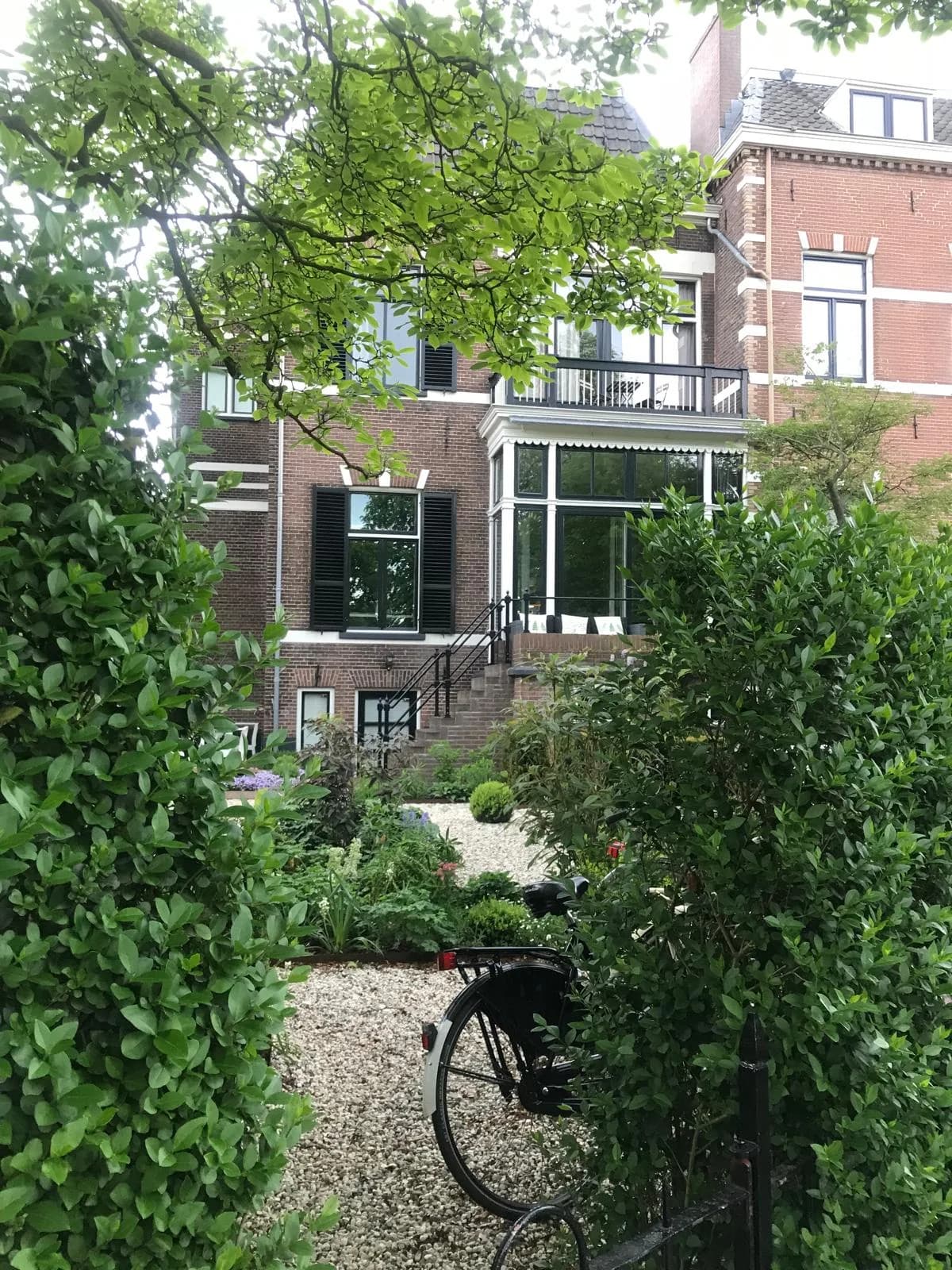 A classic Dutch townhouse surrounded by flowers and greenery with a bicycle nearby