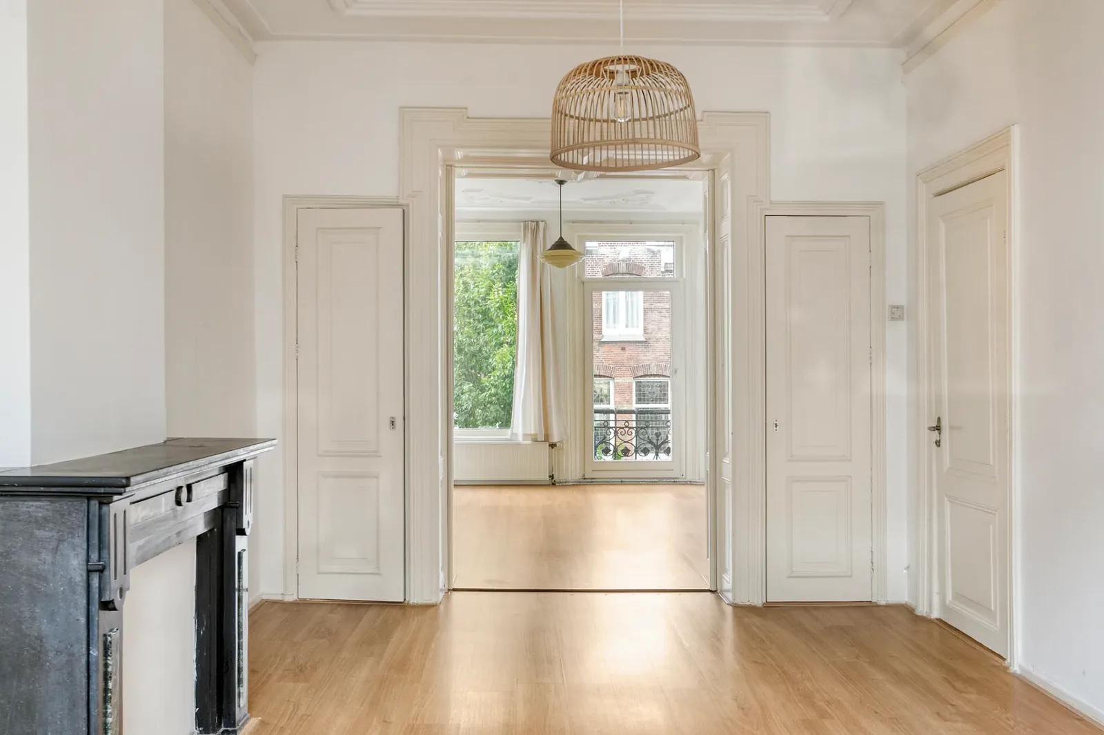 An unfurnished Dutch living room with original fireplace, white walls and wooden floors